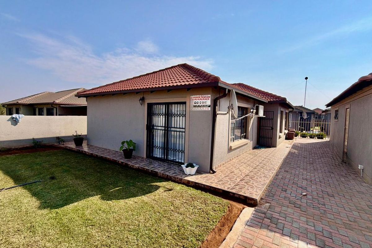 Rear view of the townhouse featuring a tiled roof, paved patio area, and a well-maintained lawn with boundary walling.