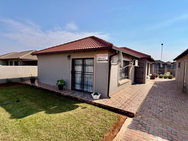 Rear view of the townhouse featuring a tiled roof, paved patio area, and a well-maintained lawn with boundary walling.