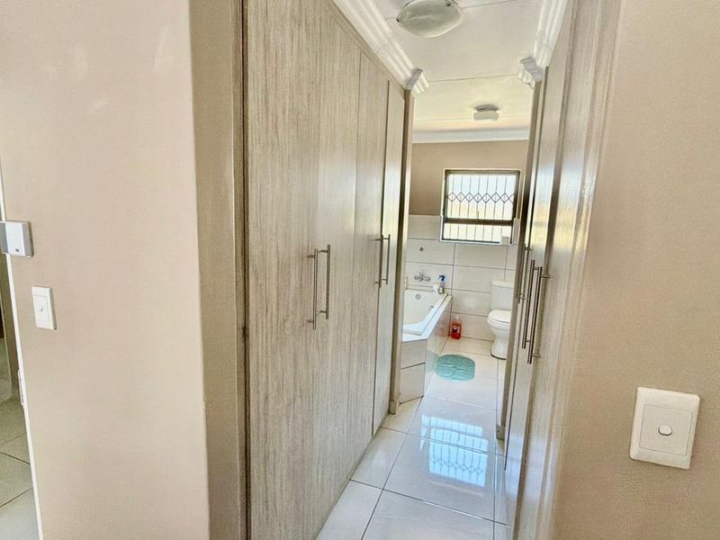 A hallway featuring built-in cupboards with wood-look finish, leading towards a bathroom with tiled floors and neutral wall tones.