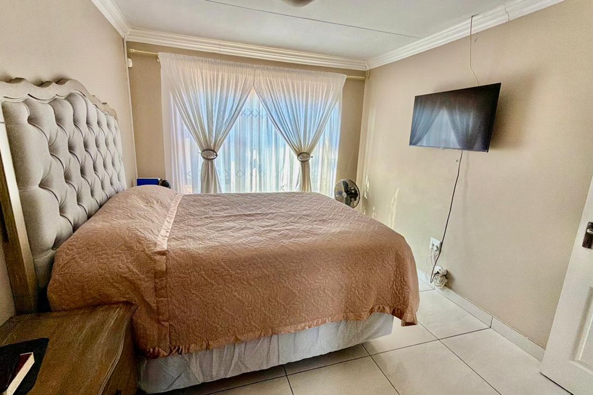 A well-lit bedroom featuring neutral wall tones, tiled flooring, and decorative crown molding, providing a comfortable and functional living space.