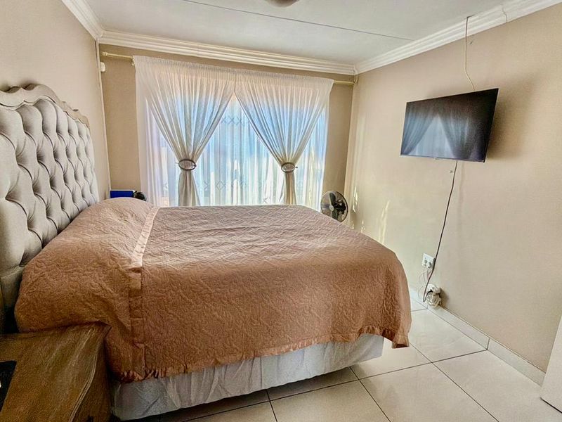 A well-lit bedroom featuring neutral wall tones, tiled flooring, and decorative crown molding, providing a comfortable and functional living space.