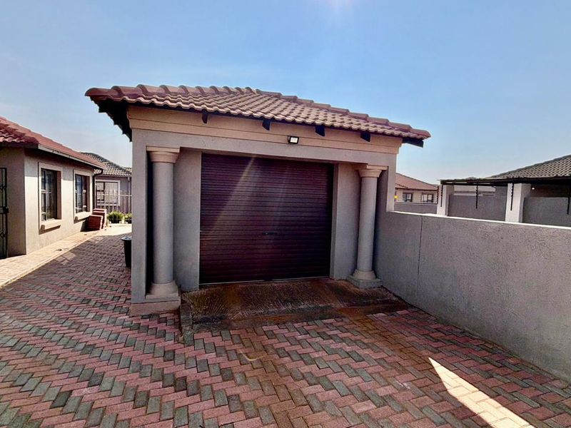 A detached single garage featuring a roll-up door, decorative columns, and a tiled roof, situated on a paved driveway within a townhouse complex.