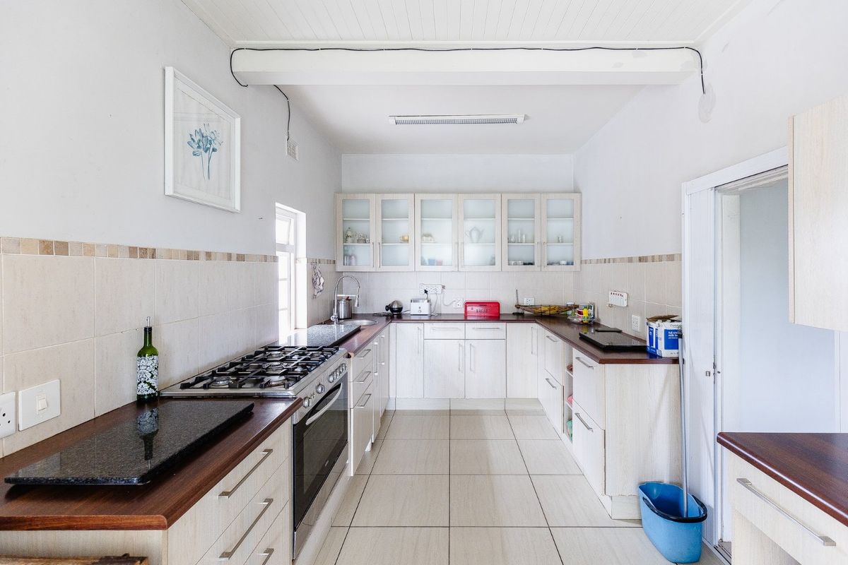 A functional kitchen featuring light-toned cabinetry, stone countertops, a gas hob, and tiled flooring, offering a practical layout for daily meal preparation.