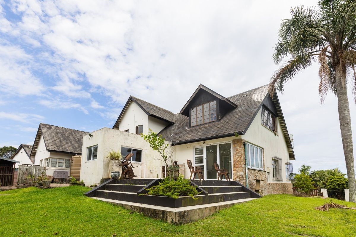 Rear view of a multi-story house featuring a raised patio, stone cladding accents, and a large garden area.
