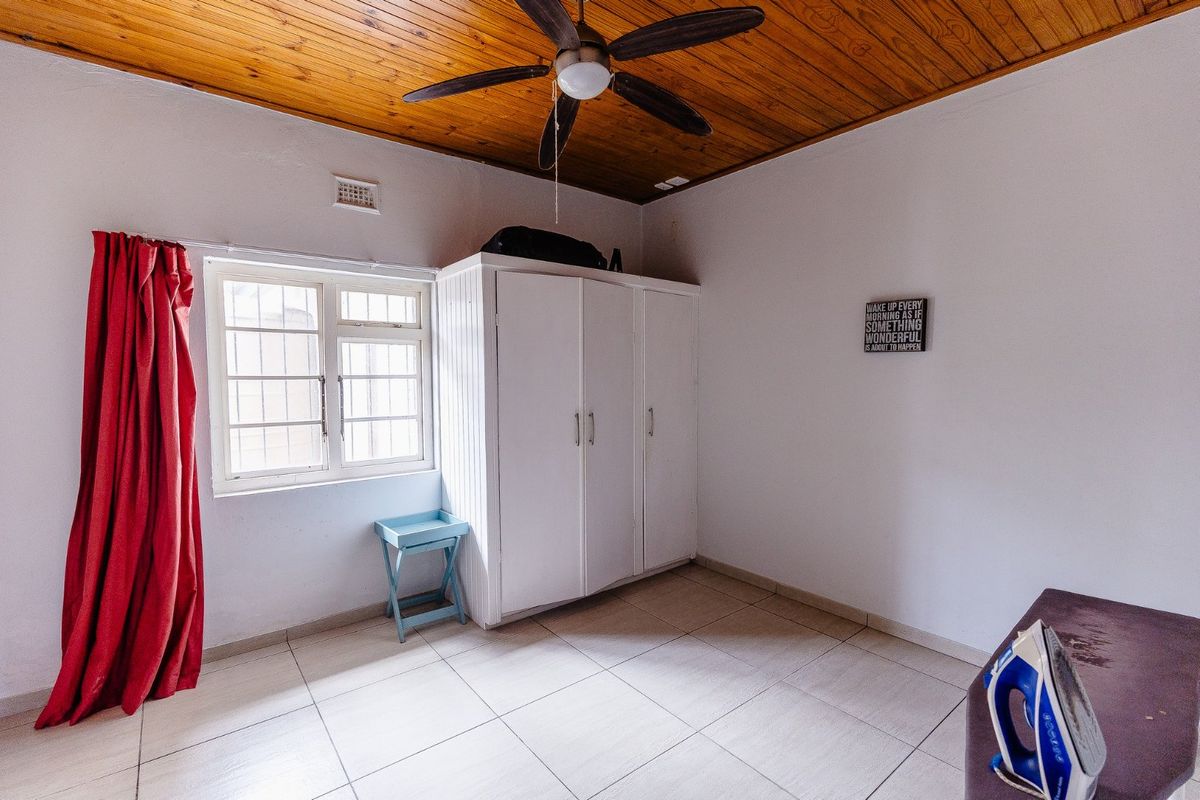 A bedroom featuring a timber-clad ceiling, ceiling fan, tiled flooring, and a built-in wardrobe with security bars on the window.