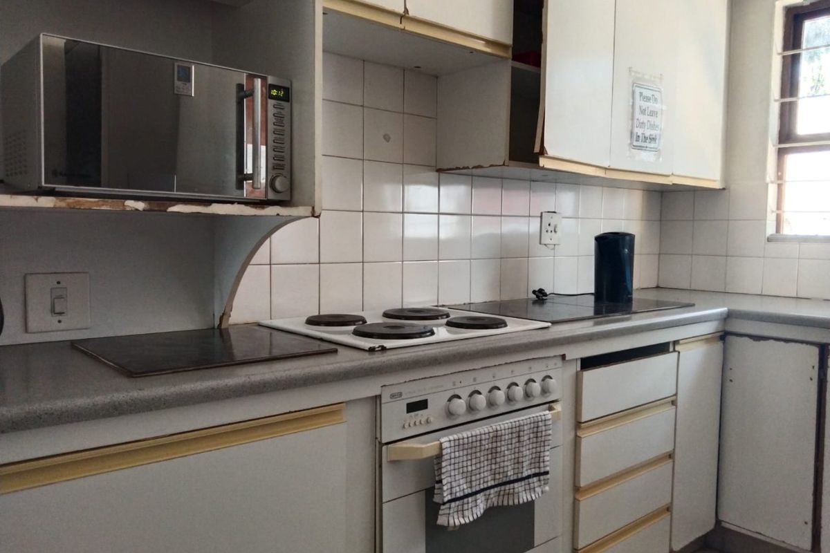 A dated kitchen featuring built-in cabinetry, an electric hob, and oven, with visible wear on the cabinet finishes and laminate countertops.