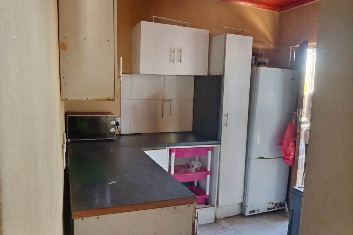 A compact kitchen featuring laminate countertops, built-in cabinetry, and a tiled splashback, requiring cosmetic updates to improve its overall condition and aesthetic appeal.