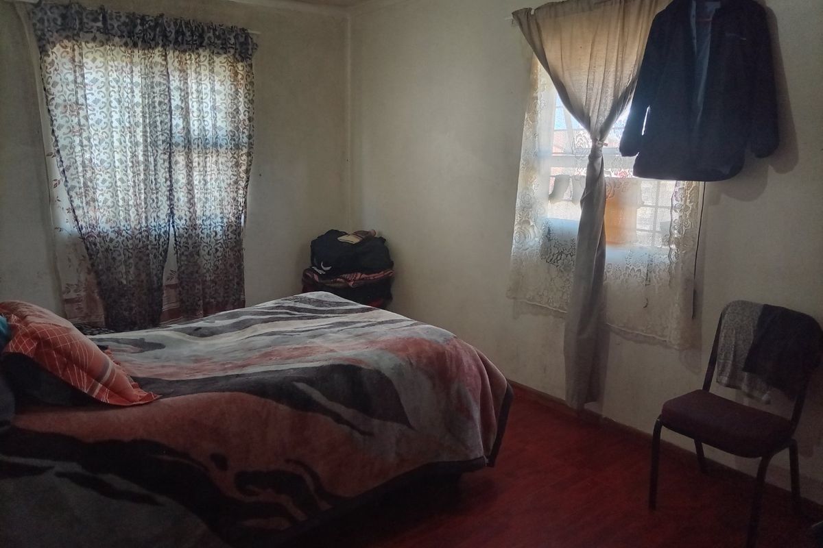 A bedroom featuring laminate flooring and windows fitted with security burglar bars.