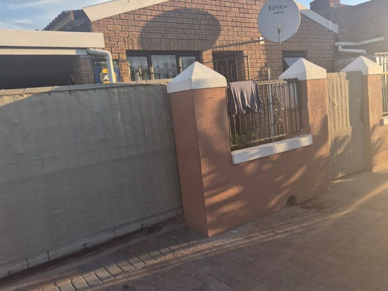 Front exterior view of a face brick house featuring a boundary wall with security gate and paved driveway access.