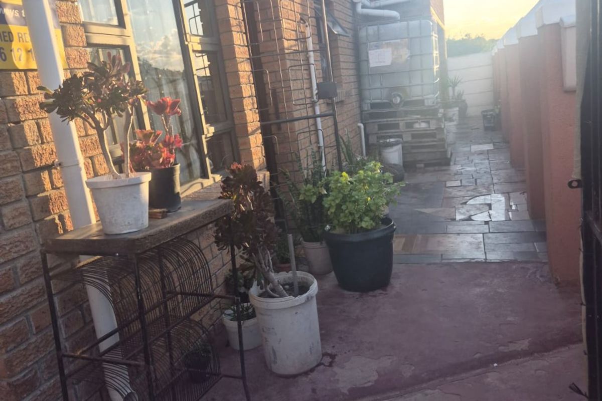 A narrow rear exterior walkway featuring brick wall construction, paved flooring, and a mounted satellite dish.