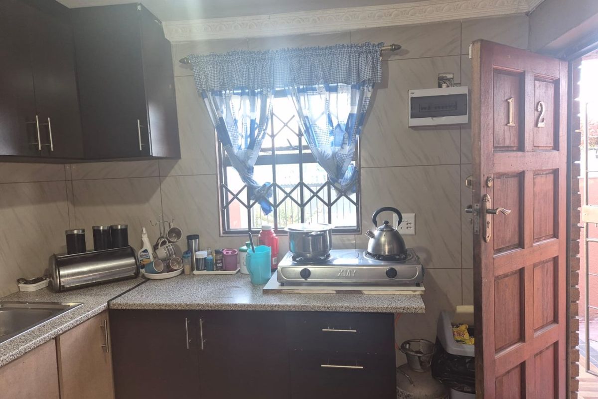 Compact kitchen featuring dark cabinetry, laminate countertops, tiled splashbacks, and a security gate entrance.