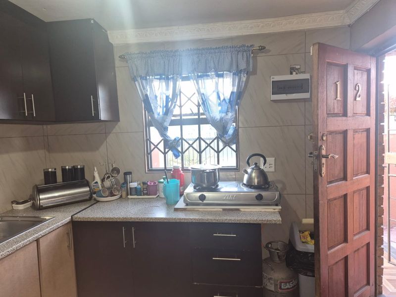 Compact kitchen featuring dark cabinetry, laminate countertops, tiled splashbacks, and a security gate entrance.