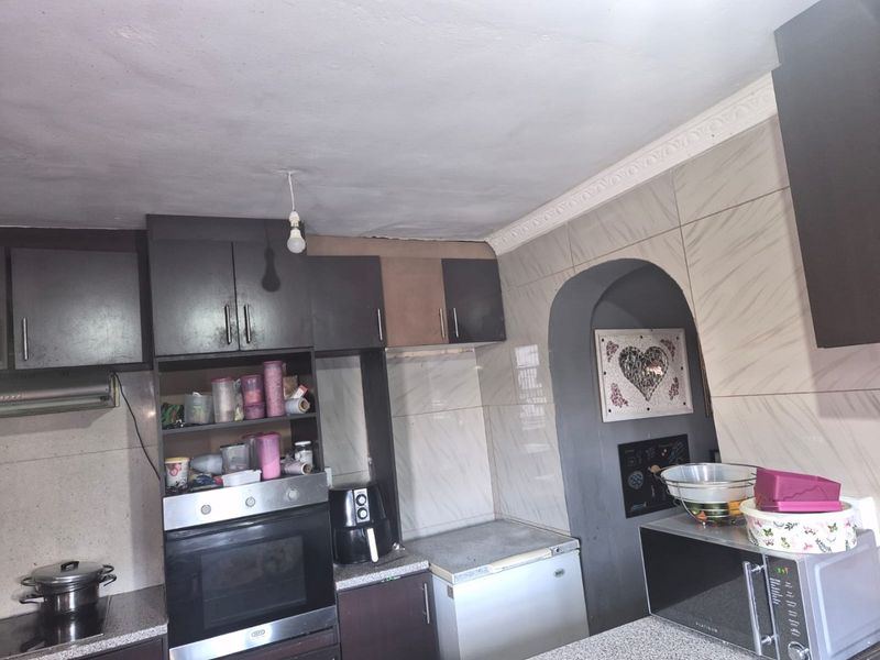 A functional kitchen featuring dark fitted cabinetry, a built-in oven, extractor fan, and a distinctive arched wall detail with tiled splashbacks.