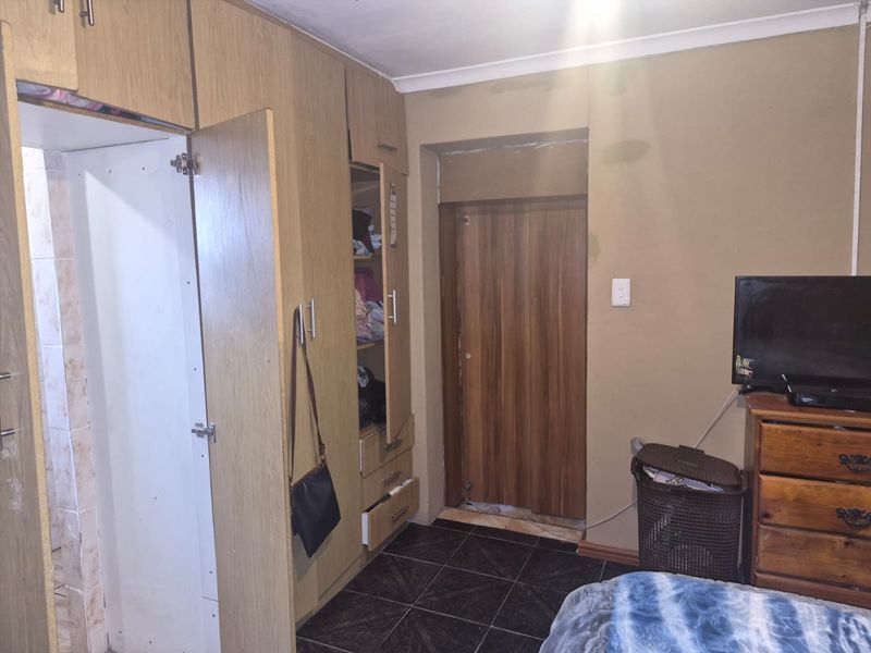 Bedroom featuring built-in wooden cupboards and dark tiled flooring, requiring cosmetic updates to the walls and door frames.