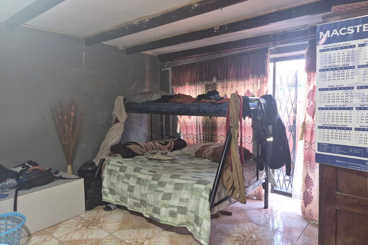 A bedroom featuring tiled flooring, exposed ceiling beams, and a sliding door with a security gate leading to the exterior.