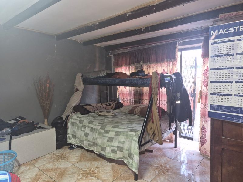 A bedroom featuring tiled flooring, exposed ceiling beams, and a sliding door with a security gate leading to the exterior.