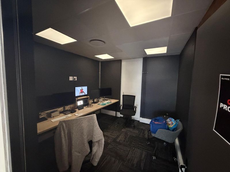 A compact, modern office space featuring dark walls, recessed ceiling lighting, and a built-in desk setup, suitable for a professional workspace.