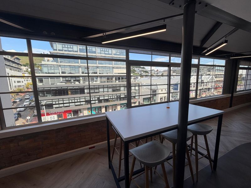 Modern office space featuring exposed brick walls, industrial steel beams, and large windows offering an expansive urban city view.