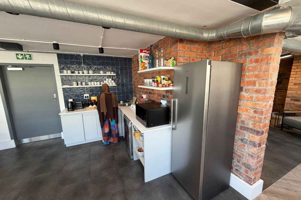 A modern industrial-style kitchenette featuring exposed brick walls, exposed ducting, tiled splashbacks, and open shelving with built-in cabinetry.