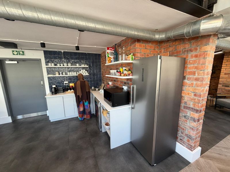 A modern industrial-style kitchenette featuring exposed brick walls, exposed ducting, tiled splashbacks, and open shelving with built-in cabinetry.