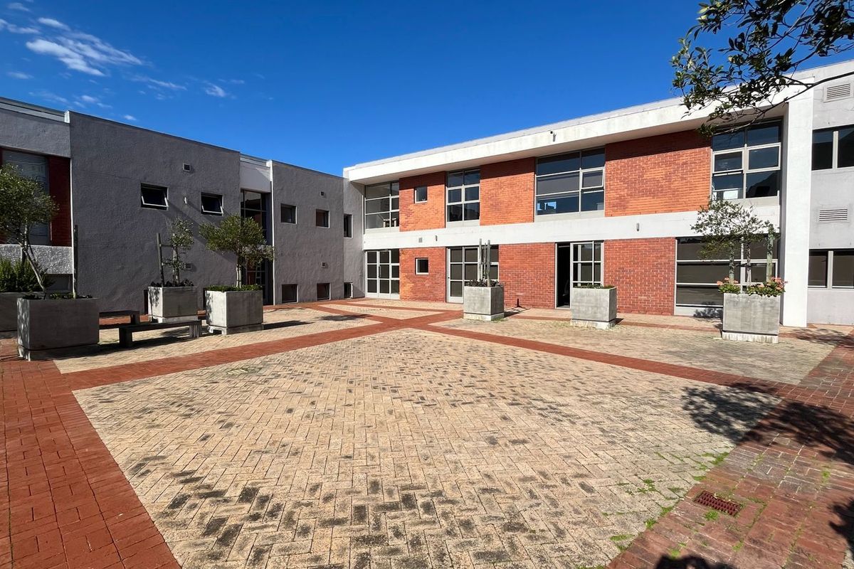 A spacious commercial courtyard featuring paved surfaces, brick and rendered facades, and integrated concrete planters, providing an open-air communal area.