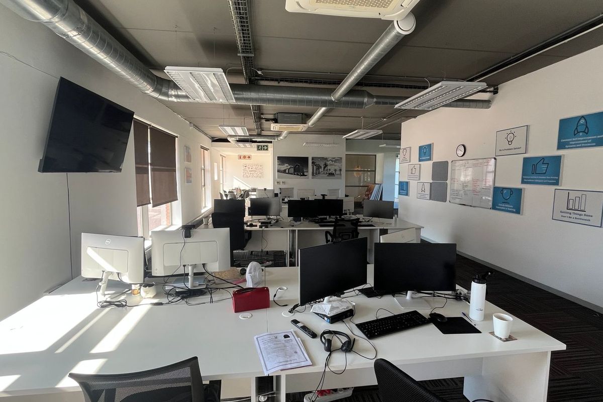 Modern open-plan commercial office space featuring exposed industrial ceilings, ducted air conditioning, and carpeted flooring, providing a functional professional work environment.