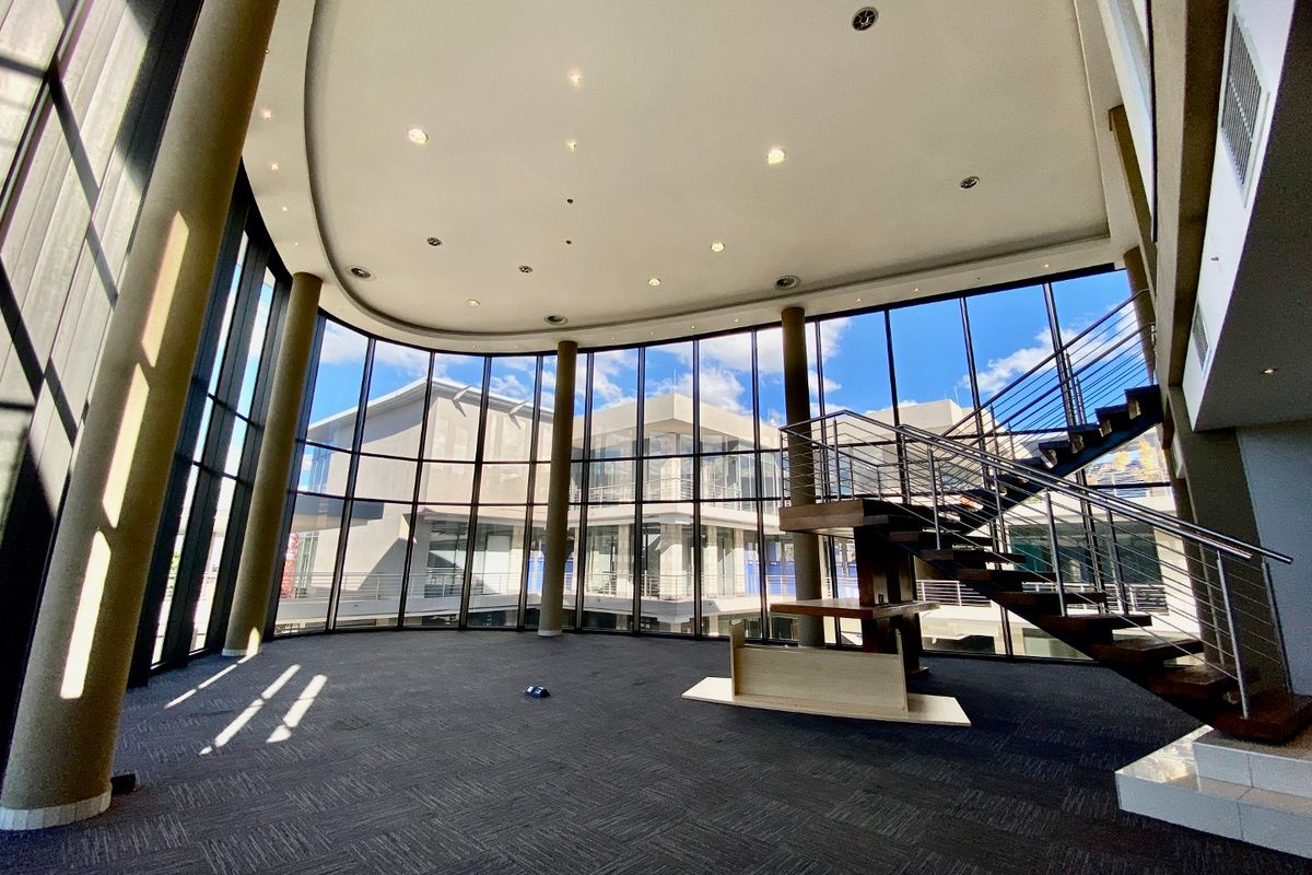 Spacious commercial entrance lobby featuring a striking floating staircase, floor-to-ceiling glass curtain walls, and modern recessed lighting.