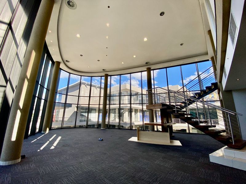 Spacious commercial entrance lobby featuring a striking floating staircase, floor-to-ceiling glass curtain walls, and modern recessed lighting.
