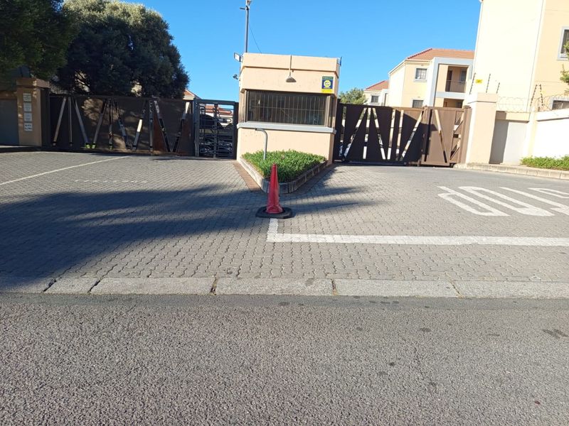 Secure apartment complex entrance featuring a gated access point, guard house, and paved driveway with electric fencing.