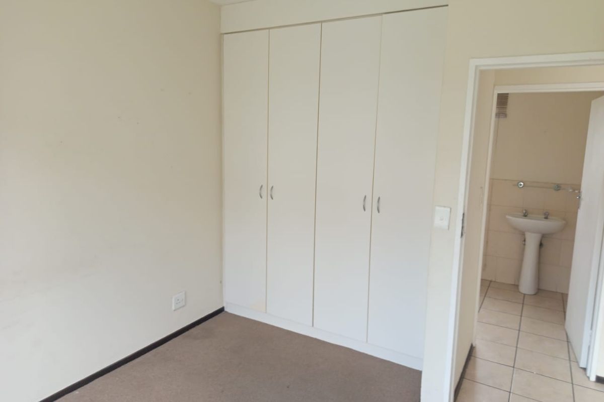 A vacant bedroom featuring built-in wardrobes, neutral carpeting, and direct access to an en-suite bathroom with a pedestal basin.