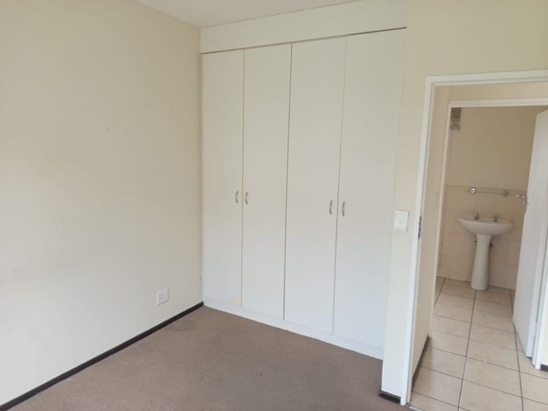 A vacant bedroom featuring built-in wardrobes, neutral carpeting, and direct access to an en-suite bathroom with a pedestal basin.
