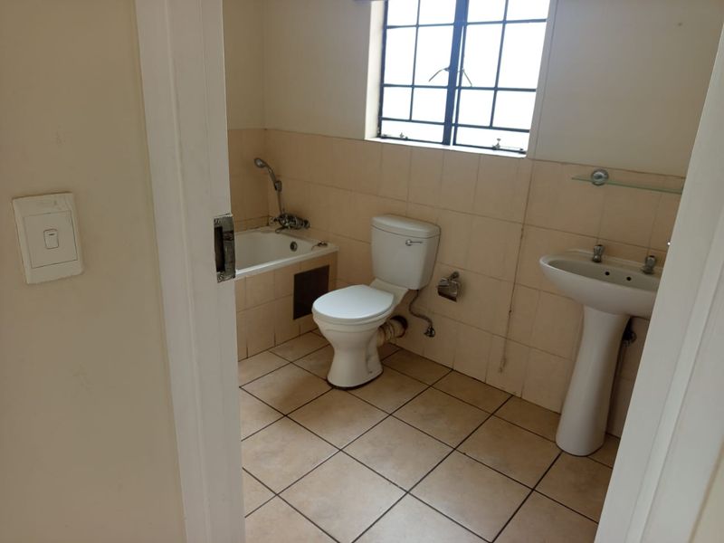 A dated bathroom featuring a pedestal basin, toilet, and built-in bathtub with tiled walls and flooring, requiring cosmetic updates.