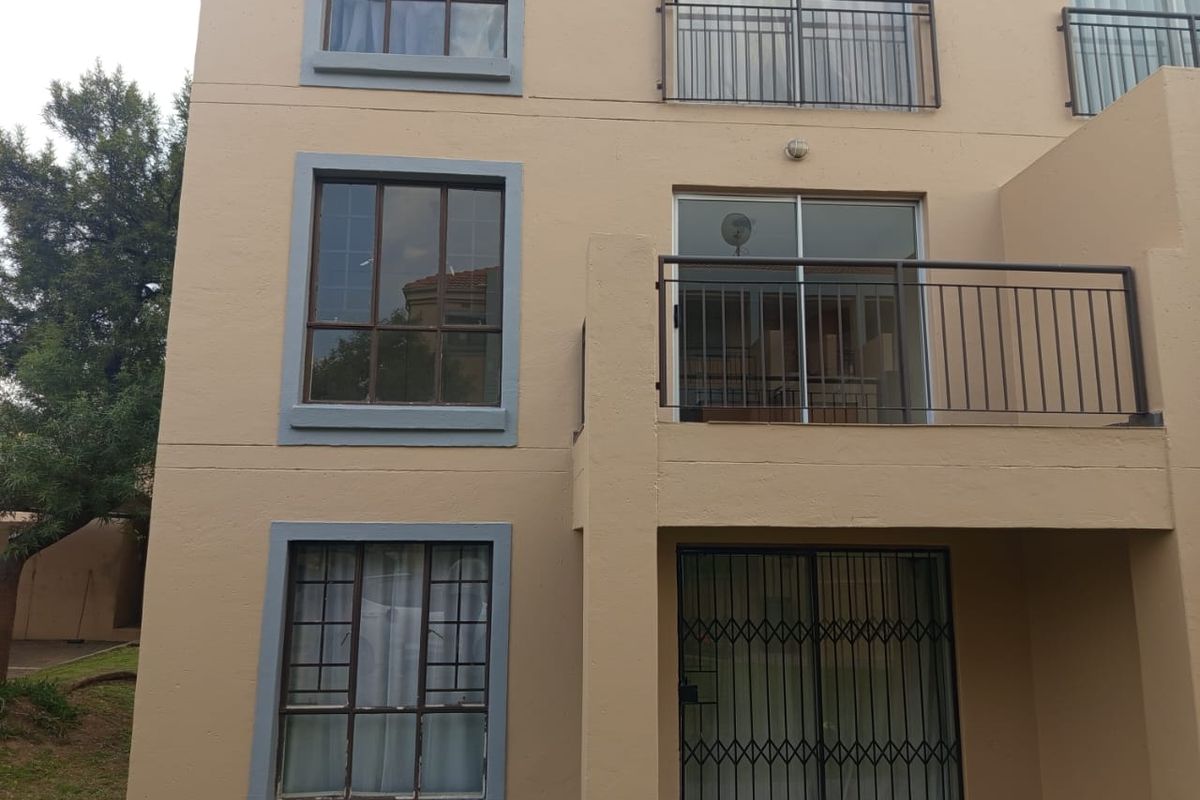 Rear exterior view of an apartment building featuring balconies with metal railings, sliding glass doors, and security gates on the ground floor.