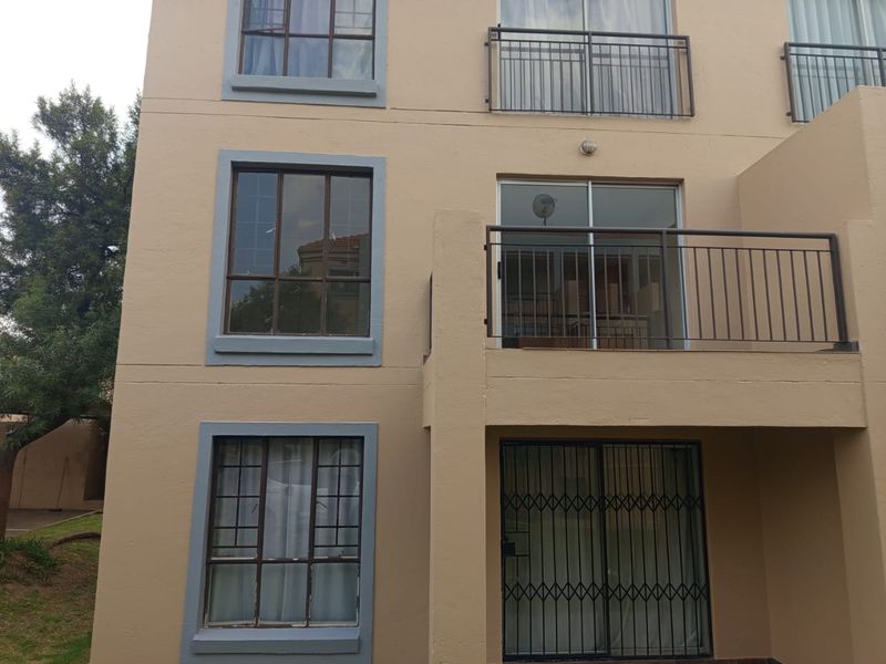 Rear exterior view of an apartment building featuring balconies with metal railings, sliding glass doors, and security gates on the ground floor.