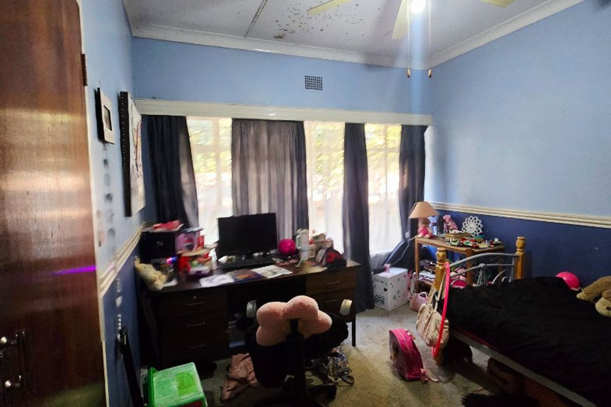 A bedroom featuring a ceiling fan, built-in wardrobe, and chair rail, currently showing significant ceiling water staining and worn flooring.
