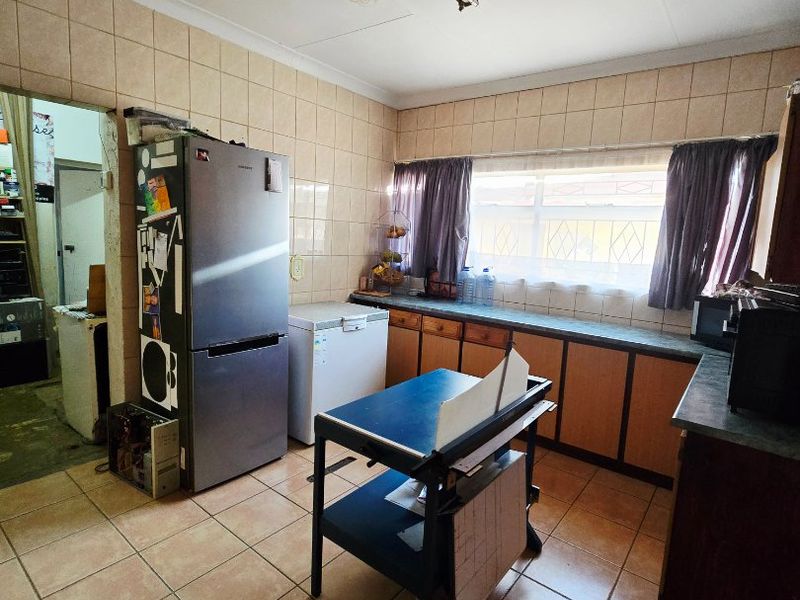 A dated kitchen featuring tiled walls and flooring, built-in cabinetry with laminate countertops, and a functional layout with an adjacent scullery area.