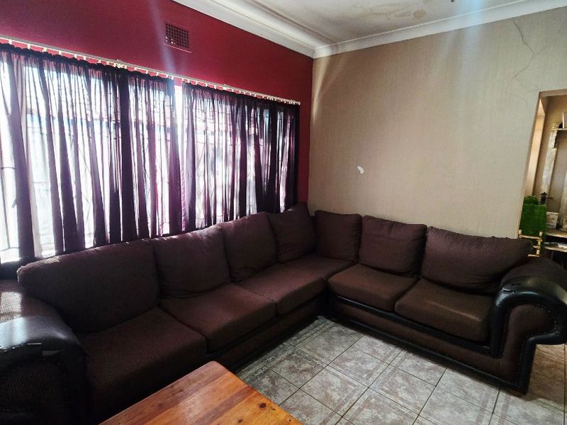 Living room featuring tiled flooring, a ceiling fan, and decorative cornicing, showing signs of ceiling water damage and wall cracking.