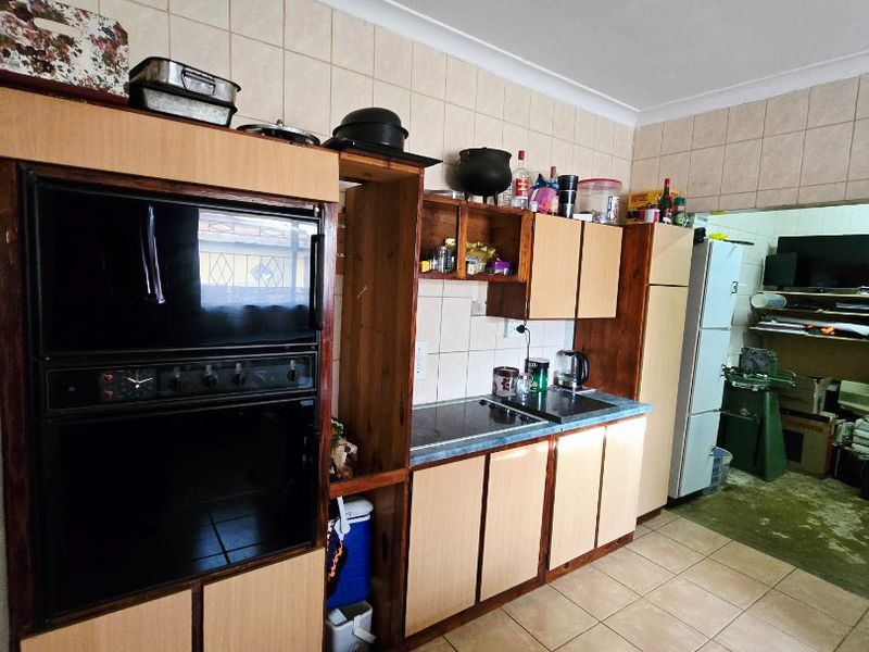 A functional kitchen featuring built-in oven and hob, tiled splashbacks, and tiled flooring, offering a dated aesthetic ready for modernization.