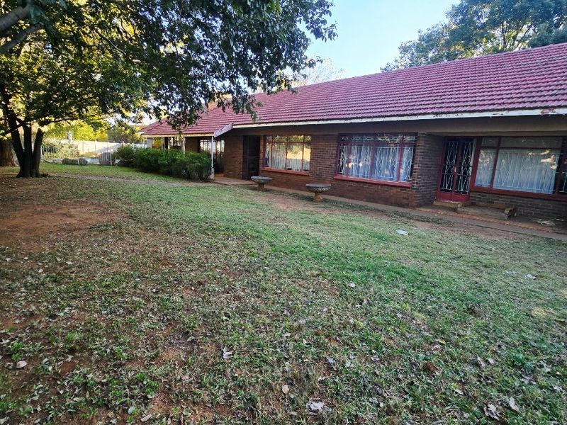 Rear view of a single-story brick house featuring a tiled roof, large windows, and security gates, set within a spacious garden area.