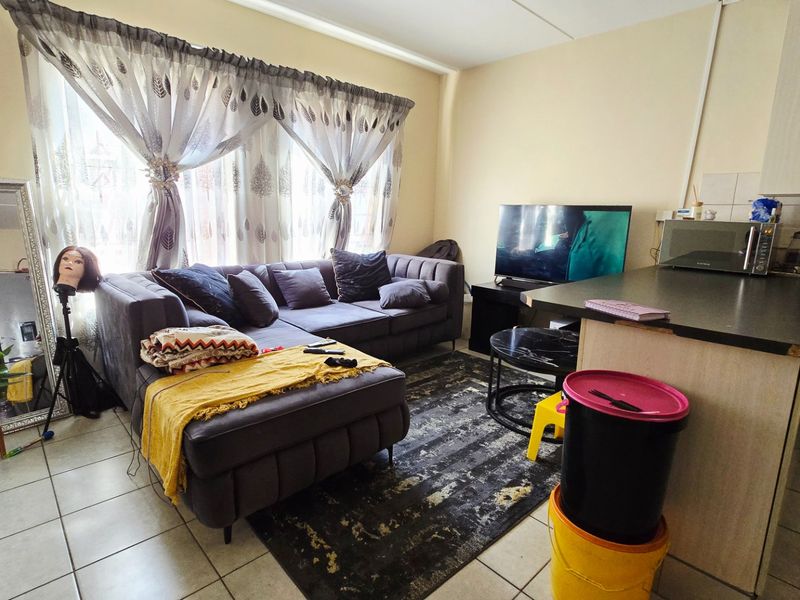 Open-plan living area featuring tiled flooring and a functional kitchen with built-in cabinetry and oven, creating a combined living and cooking space.