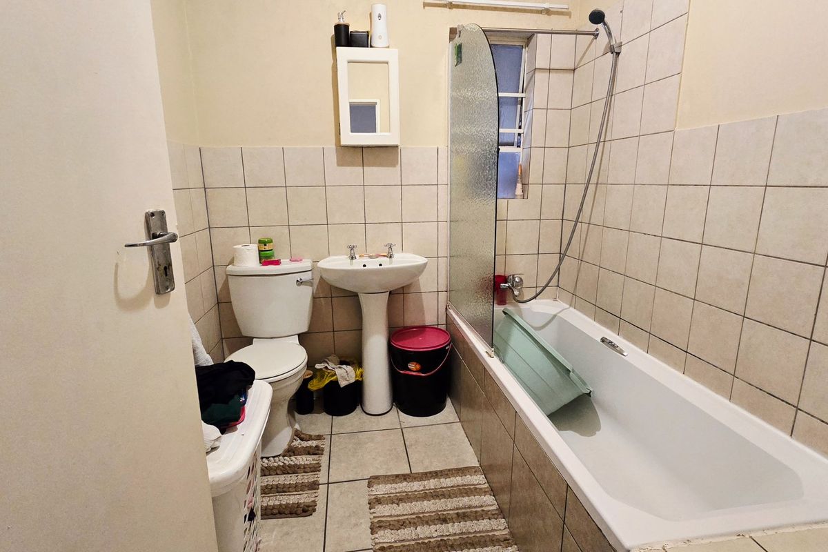 A functional bathroom featuring a pedestal basin, toilet, and a bathtub with a glass shower screen and wall-to-floor tiling.