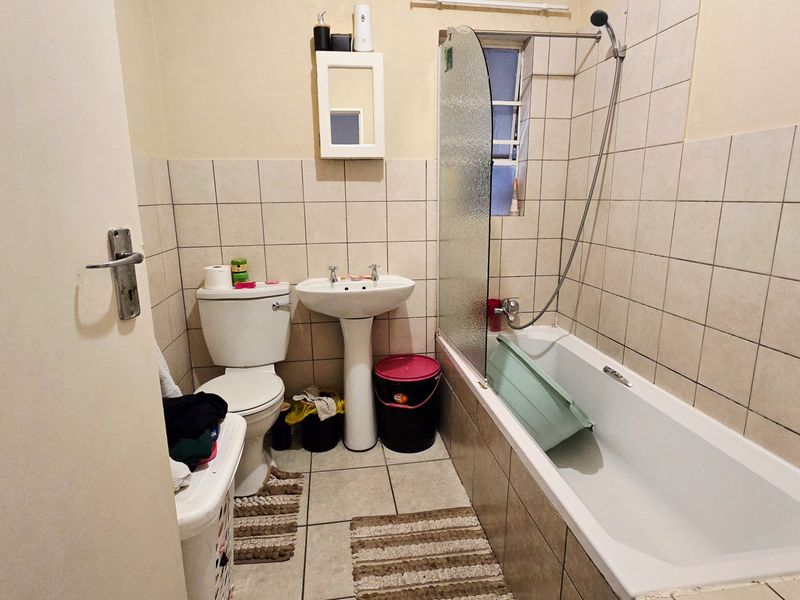 A functional bathroom featuring a pedestal basin, toilet, and a bathtub with a glass shower screen and wall-to-floor tiling.