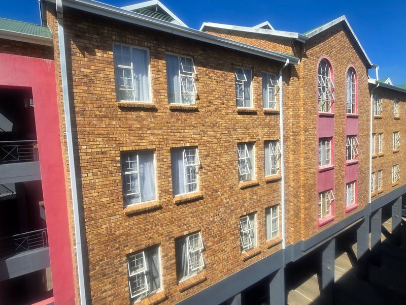 Exterior view of a multi-story apartment building featuring face brick construction, casement windows, and a covered ground-level parking area.