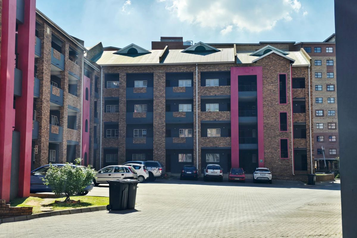 Exterior view of a multi-story apartment complex featuring brick facade, private balconies, and a paved parking area.