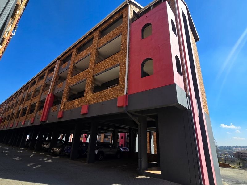 Exterior view of a multi-story apartment building featuring a brick facade, covered ground-level parking, and private balconies.