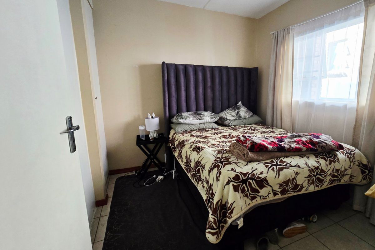 A compact bedroom featuring tiled flooring and a built-in cupboard, providing a functional sleeping space with natural light from the window.