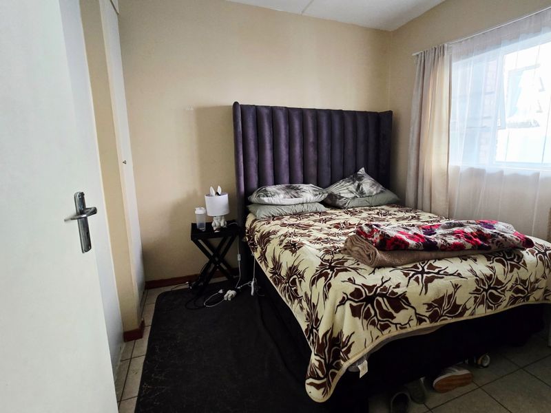 A compact bedroom featuring tiled flooring and a built-in cupboard, providing a functional sleeping space with natural light from the window.