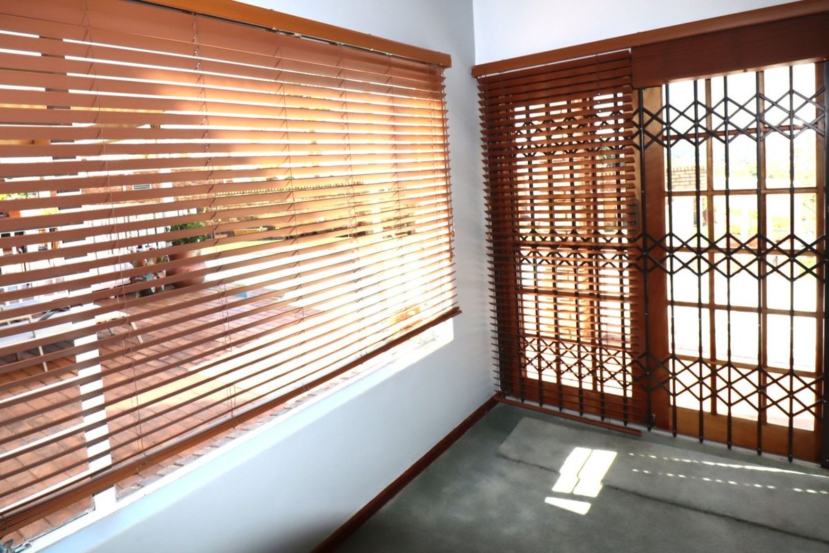 A bright, empty living area featuring wooden venetian blinds and a secure sliding glass door leading to an outdoor patio space.
