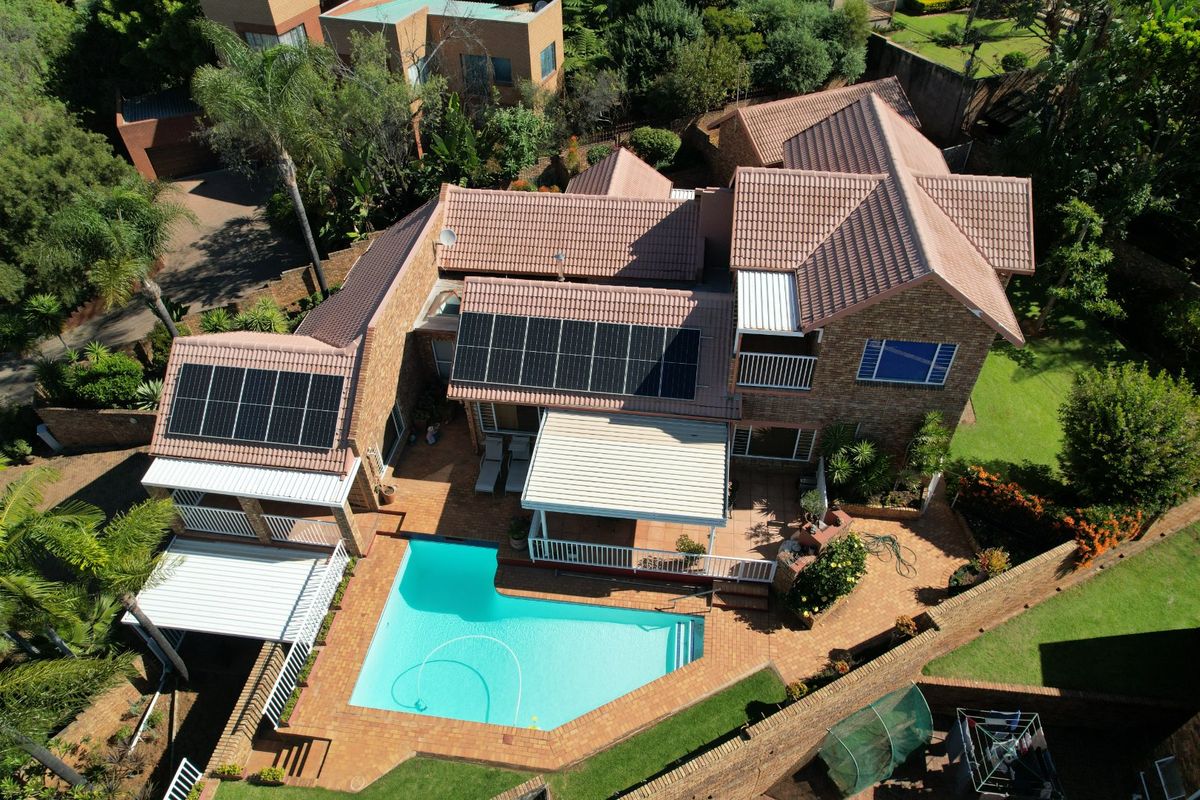 Aerial view of a residential property featuring a tiled roof with solar panels, a swimming pool, and paved patio areas with retractable awnings.