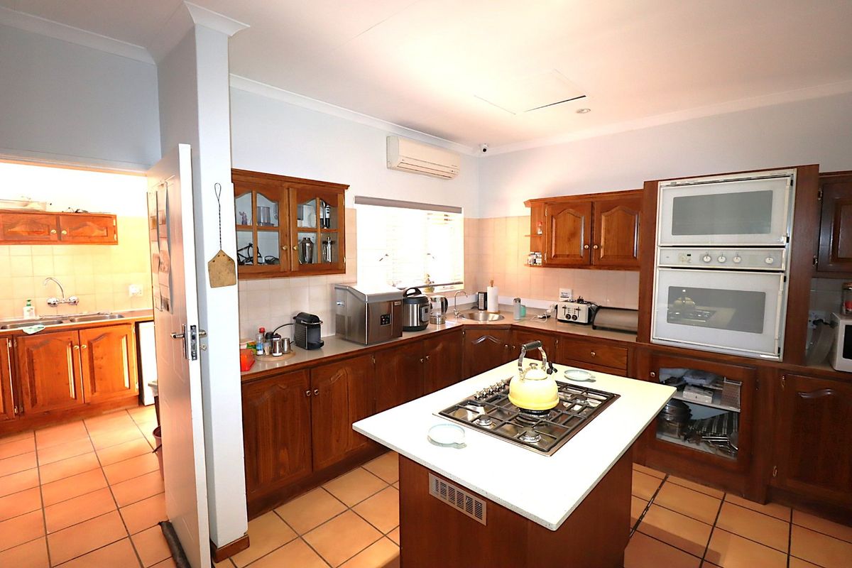 A spacious kitchen featuring traditional wooden cabinetry, a central island with a gas hob, built-in oven, and tiled flooring, with an adjacent scullery area.